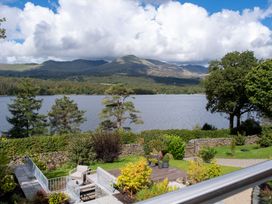 A view of a lake and mountains with trees and a patio at Deer Close in Coniston
