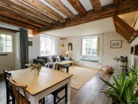 A living room with wooden beams on the ceiling a wooden dining table with chairs a gray sofa and two large windows at The Stables at Daubeneys Colerne