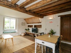 A living room with wooden beams a window seat a coffee table a dining table with flowers and a television at The Stables at Daubeneys Colerne