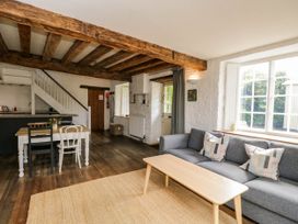 A living room with a gray sofa and wooden coffee table next to a dining table with mismatched chairs and exposed wooden beams at The Stables at Daubeneys Colerne