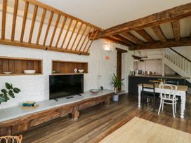 A living room and kitchen area with wooden beams a television on a long wooden bench and a dining table with mismatched chairs at The Stables at Daubeneys Colerne