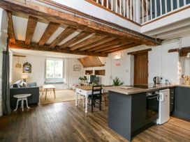 An open-plan living area with exposed wooden beams a dining table a kitchen island with oven and refrigerator a sofa and window seating at The Stables at Daubeneys in Colerne