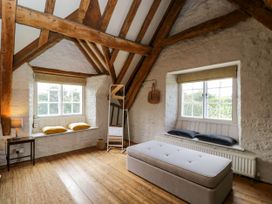 A bedroom with wooden beams white brick walls two windows with cushions and a bench at The Stables at Daubeneys Colerne