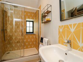 A bathroom with a shower enclosure featuring yellow patterned tiles a sink and a wall-mounted shelf at The Stables at Daubeneys Colerne