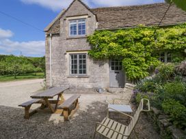 An outdoor seating area with a wooden picnic table and two metal chairs with a small table outside a stone house with greenery at The Stables at Daubeneys Colerne