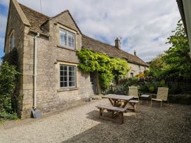 An outdoor patio area with wooden picnic table benches and two metal chairs next to a stone cottage with greenery climbing the wall at The Stables at Daubeneys Colerne