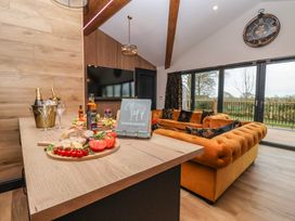 A living room with orange sofas wooden table with food and drinks large clock on wall and doors to garden at Routhorpe Lodge in Bainton near Great Driffield