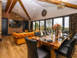 A dining area with a wooden table set with glasses and napkins next to a living area with mustard sofas and a large wall clock at Routhorpe Lodge in Bainton near Great Driffield