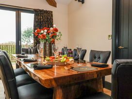 A dining room with a wooden table set with black chairs glasses and a flower vase at Routhorpe Lodge in Bainton near Great Driffield