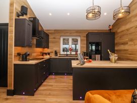 A kitchen with dark cabinets wooden countertops and walls a window above the sink and a kitchen island with a champagne bottle and glasses at Routhorpe Lodge Bainton near Great Driffield