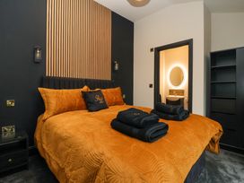 A bedroom with an orange bedspread and pillows two folded black towels on the bed a wooden panel behind the bed and a bathroom with a lit oval mirror visible at Routhorpe Lodge in Bainton near Great Driffield