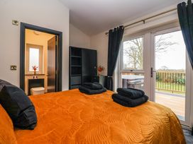 A bedroom with an orange bedspread black pillows folded towels a black cabinet and a door leading to a balcony at Routhorpe Lodge in Bainton near Great Driffield