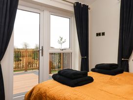 A bedroom with an orange bedspread and black towels on the bed next to glass doors with black curtains at Routhorpe Lodge in Bainton near Great Driffield
