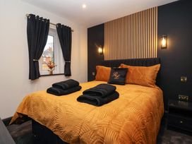 A bedroom with a bed covered in an orange quilt and black towels beside a window with black curtains at Routhorpe Lodge in Bainton near Great Driffield
