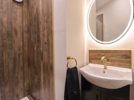 A bathroom with a white sink and brass faucet under a round mirror and wooden wall panel at Routhorpe Lodge in Bainton near Great Driffield