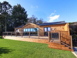 A wooden cabin with large glass windows and a deck with railings on a grassy lawn at Routhorpe Lodge in Bainton near Great Driffield