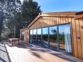An outdoor wooden deck with a table and large glass sliding doors on a wooden building at Routhorpe Lodge in Bainton near Great Driffield
