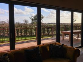 A room with a sofa facing large sliding glass doors showing a wooden deck and outdoor table at Routhorpe Lodge in Bainton near Great Driffield