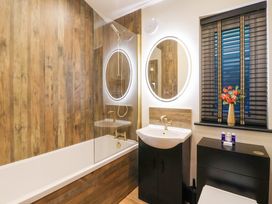 A bathroom with a bathtub shower and sink with mirror next to a window with blinds and a cabinet at Routhorpe Lodge in Bainton near Great Driffield