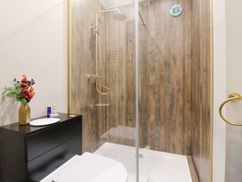 A bathroom with a glass shower enclosure wood panel walls a black cabinet with toiletries and flowers at Routhorpe Lodge in Bainton near Great Driffield