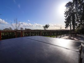 An outdoor wooden deck with a covered hot tub and a bench with trees and a hedge in the background at Routhorpe Lodge in Bainton near Great Driffield