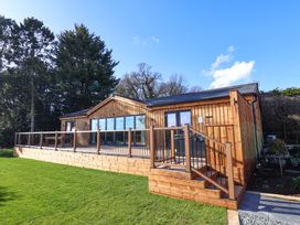 A wooden cabin with large windows and a deck surrounded by railings on a grassy area at Routhorpe Lodge in Bainton near Great Driffield