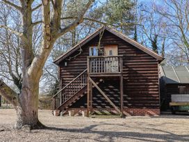 Exterior of a wooden lodge with stairs leading to a balcony and door surrounded by trees at Woodland Retreat Lodge in Brundish near Laxfield