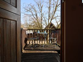 A wooden balcony with a small metal table and two metal chairs with two cups on the table at Woodland Retreat Lodge in Brundish near Laxfield