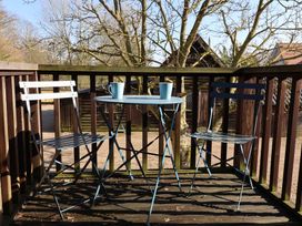 A wooden balcony with two metal chairs and a small round table with two mugs at Woodland Retreat Lodge Brundish near Laxfield