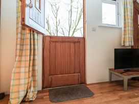 An open wooden stable door with a window and curtains next to a television on a wooden floor at Woodland Retreat Lodge in Brundish near Laxfield