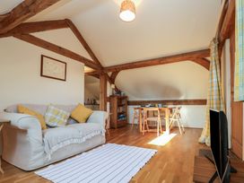 A living room with a sofa, a dining table with chairs, a television, wooden beams, and a rug at Woodland Retreat Lodge in Brundish near Laxfield