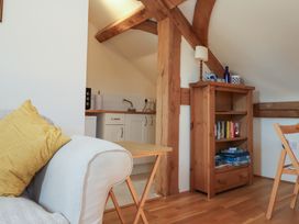 A corner of a living area with a sofa and yellow cushion a small wooden table a wooden bookshelf and part of a kitchenette at Woodland Retreat Lodge in Brundish near Laxfield