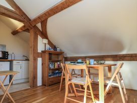 A dining area with wooden table and chairs next to a small kitchen and wooden bookshelf at Woodland Retreat Lodge in Brundish near Laxfield