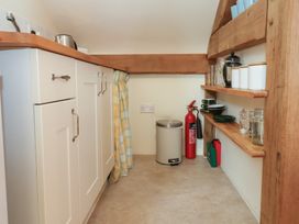 A small kitchen area with white cabinets wooden shelves a trash bin and a fire extinguisher at Woodland Retreat Lodge Brundish near Laxfield