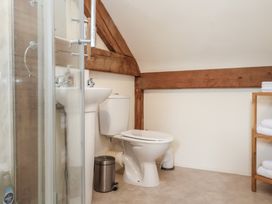 A bathroom with a shower enclosure sink toilet a metal trash bin and a wooden shelf with towels at Woodland Retreat Lodge in Brundish near Laxfield
