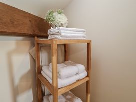 A wooden shelving unit with folded white towels and a vase with white flowers at Woodland Retreat Lodge in Brundish near Laxfield
