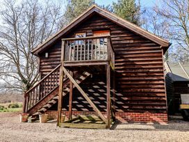 A wooden cabin with a balcony and stairs outside with trees in the background at Woodland Retreat Lodge in Brundish near Laxfield