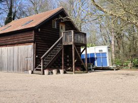 A wooden building with an external staircase and a blue and white trailer parked beside it surrounded by trees at Woodland Retreat Lodge in Brundish near Laxfield