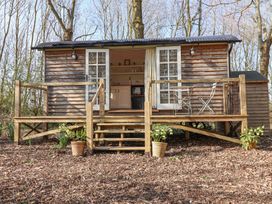 A wooden shepherds hut with open double doors and a small porch with steps and a metal table and chairs at Woodlands Retreat Shepherds Hut Brundish near Laxfield