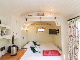 A small bedroom with a double bed pillows and towels next to a kitchenette with appliances and floral curtains at Woodlands Retreat Shepherd's Hut Brundish near Laxfield