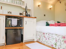 A kitchenette area with a black microwave and mini fridge next to a bed with floral bedding and pink towels at Woodlands Retreat Shepherd's Hut Brundish near Laxfield