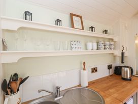 A kitchen countertop with a sink a paper towel holder a kettle and a toaster below shelves with glasses mugs and small lanterns at Woodlands Retreat Shepherd's Hut Brundish near Laxfield