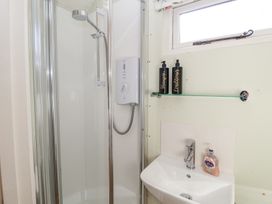A bathroom with a corner shower unit a sink with a faucet and soap dispenser and a shelf holding shampoo and conditioner at Woodlands Retreat Shepherd's Hut in Brundish near Laxfield