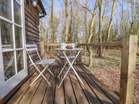 A wooden deck with two white metal chairs and a small round table with mugs and croissants in a wooded area at Woodlands Retreat Shepherd's Hut Brundish near Laxfield