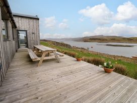 An outdoor wooden deck with a picnic table and potted plants overlooking a body of water at WildLuing Cullipool Isle Of Luing