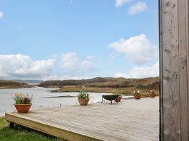 A wooden deck with flower pots and a fire pit overlooking a water body and hills at WildLuing in Cullipool Isle Of Luing