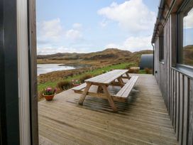 A wooden deck with a picnic table and flower pots overlooking a lake and hills at WildLuing in Cullipool Isle Of Luing