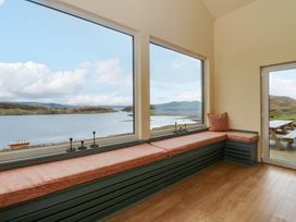 A room with built in seating and cushions next to large windows overlooking a body of water and a door leading outside at WildLuing Cullipool Isle Of Luing