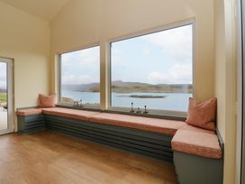 A room with a long cushioned bench under large windows overlooking water and hills at WildLuing Cullipool Isle Of Luing