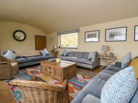 A living room with three gray sofas a wooden coffee table wicker chairs and framed pictures on the wall at WildLuing in Cullipool Isle Of Luing